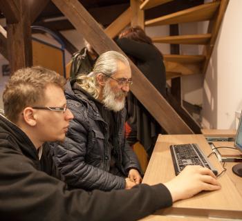 a young volunteer teaches an older, homeless man to use a computer in the library