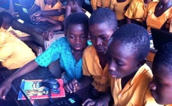 Ghanaian children in a classroom crowding around a computer.