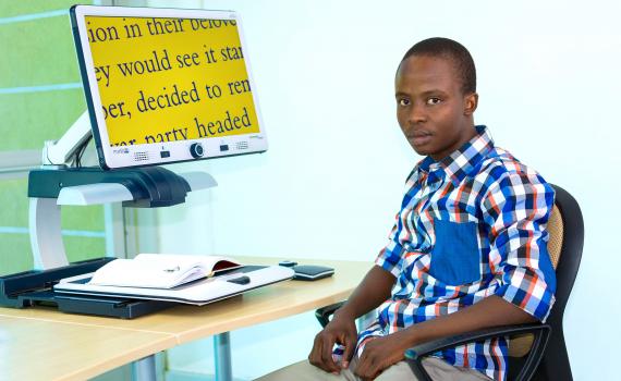 Young man, Gorata Matome, using large print on a computer screen. He is looking directly at the camera. Young man, Gorata Matome, using large print on a computer screen.